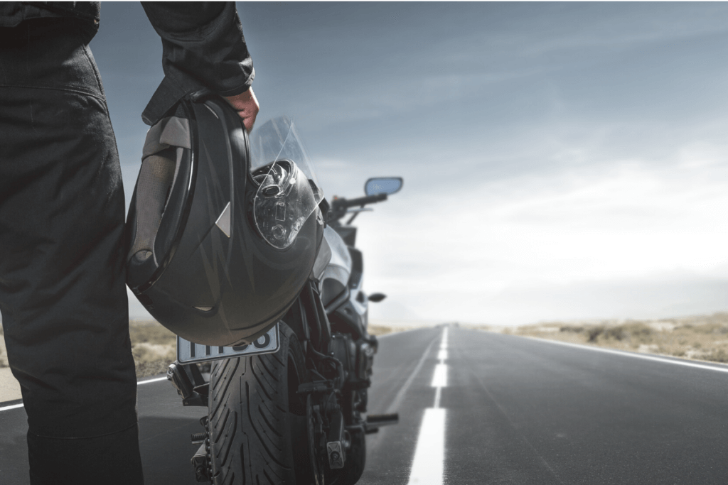 Man holding a helmet next to a motorcycle on the open road