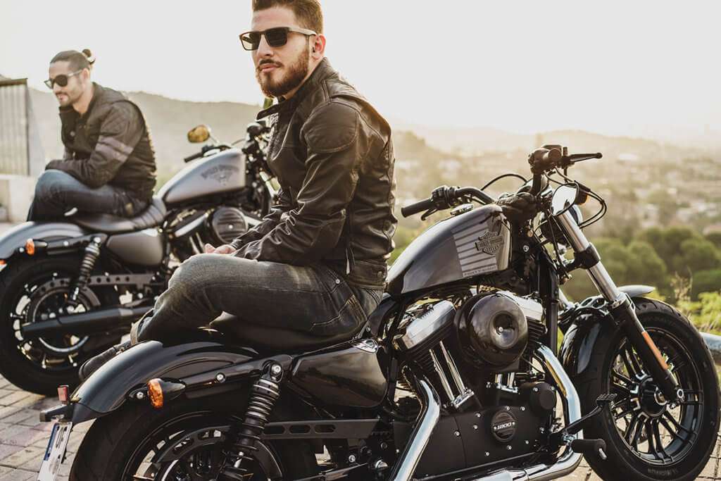 2 men each sitting on a Harley Davidson motorcycle wearing jeans