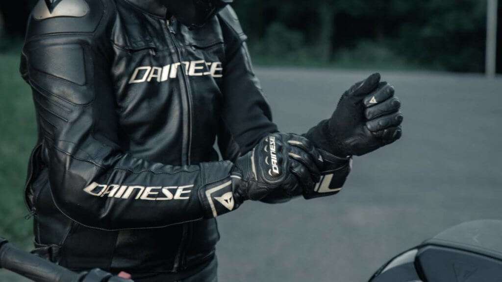 Man in black leather motorcycle jacket putting on black Dainese gloves