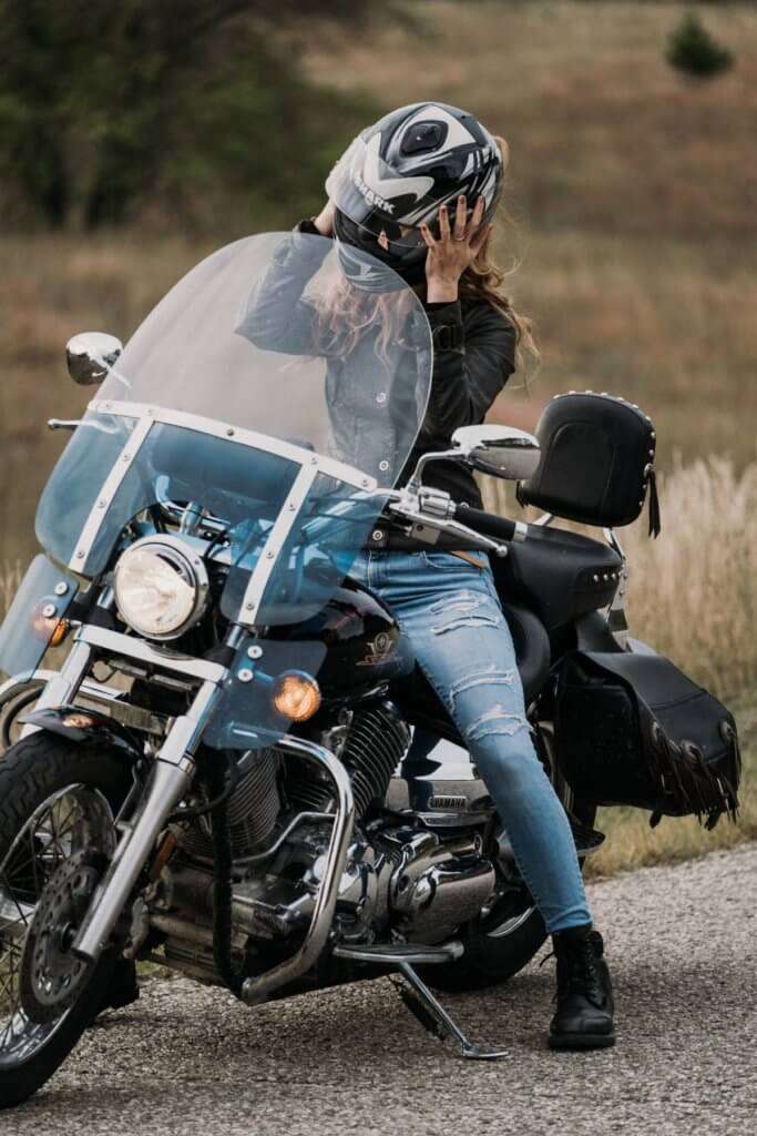 Woman taking off her helmet on a black motorcycle with a windshield