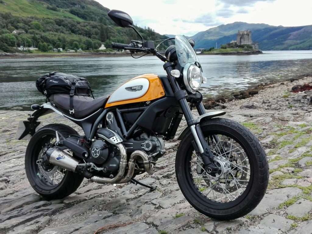 Yellow motorcycle with fly screen in front of a lake