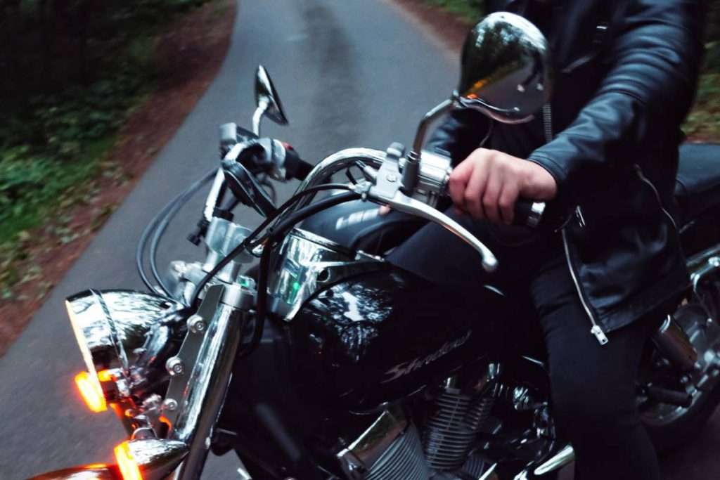 Person on black motorcycle holding handlebars with 1 hand